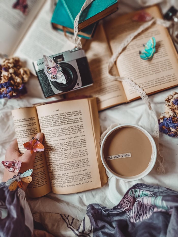 hero-img-02 A warm, artistic scene featuring an open book, cozy cup of coffee, and a vintage camera adorned with butterflies.