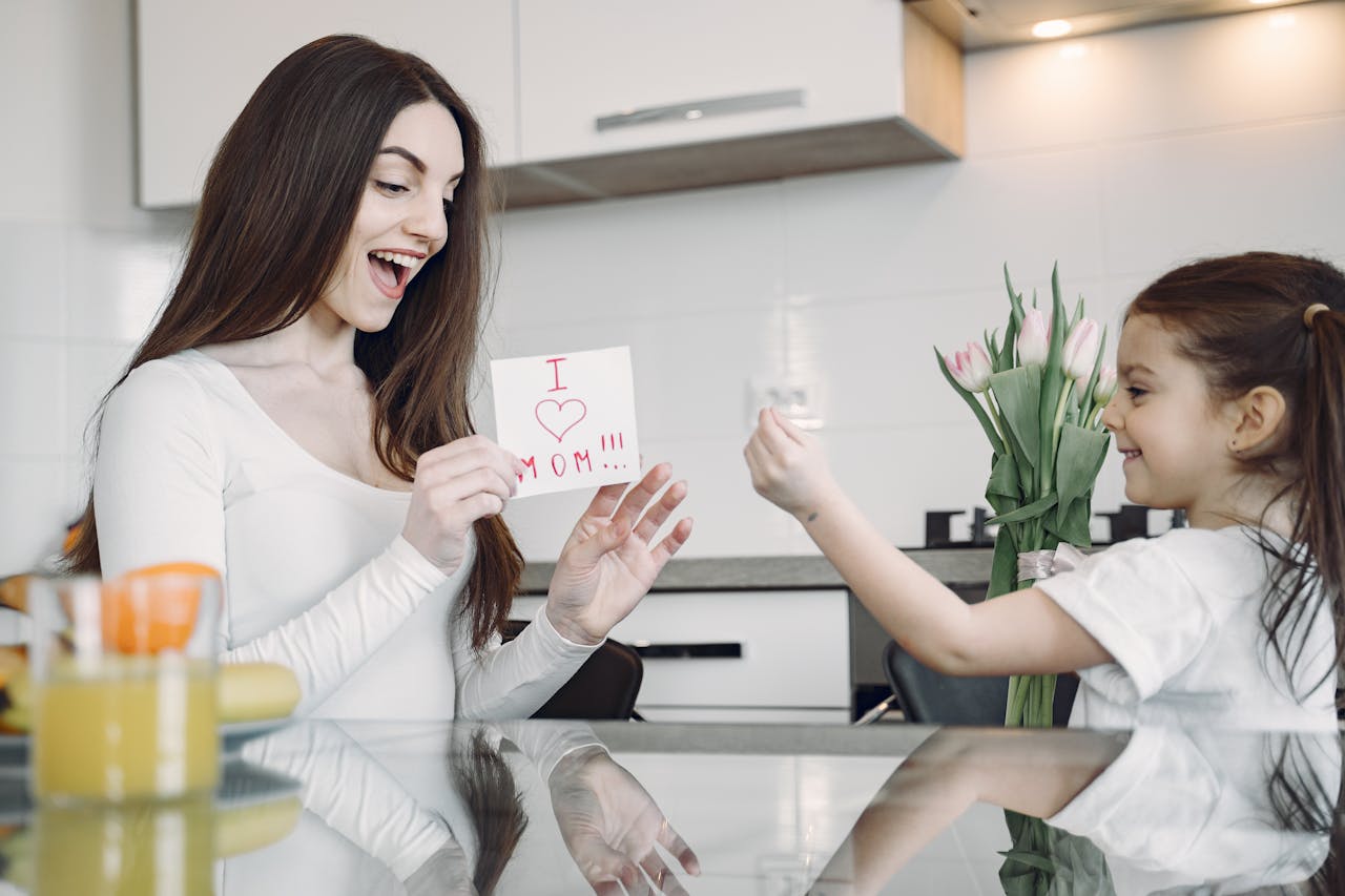 about-01 A mother and daughter sharing a joyful moment with flowers and a card in a kitchen.