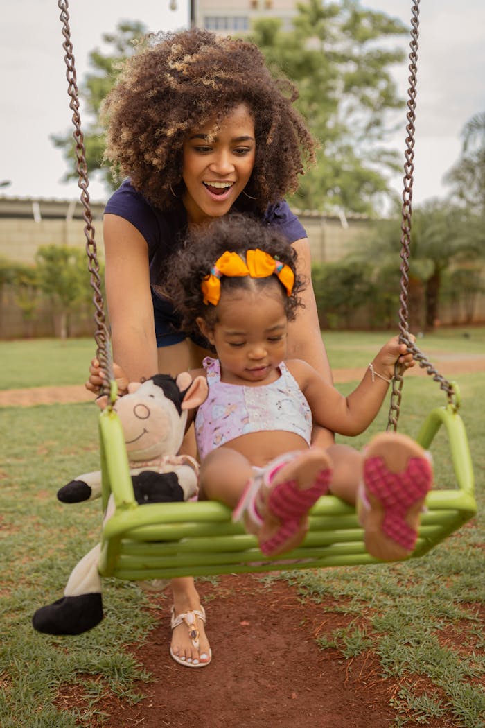 services-01 Delightful moment captured of a mother pushing her daughter on a swing in a sunny park.