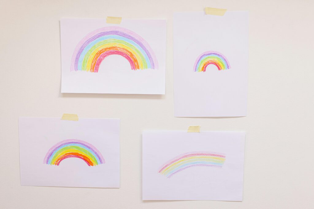 Four hand-drawn rainbow illustrations taped on a wall, creating a vibrant and cheerful display.